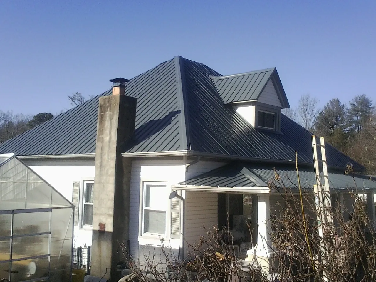 Dark blue standing seam metal roof on a white farmhouse with dormer — Slate & Tile Roof Repair by Roofing Brothers in Peshtigo