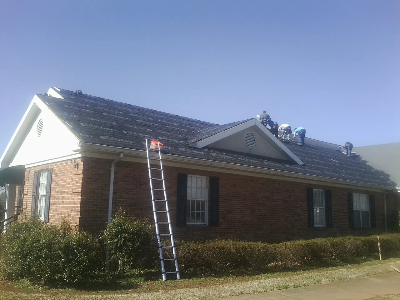 Crew tearing shingles off a brick ranch roof with a ladder set — Metal Roof Repair work by our crew in Peshtigo