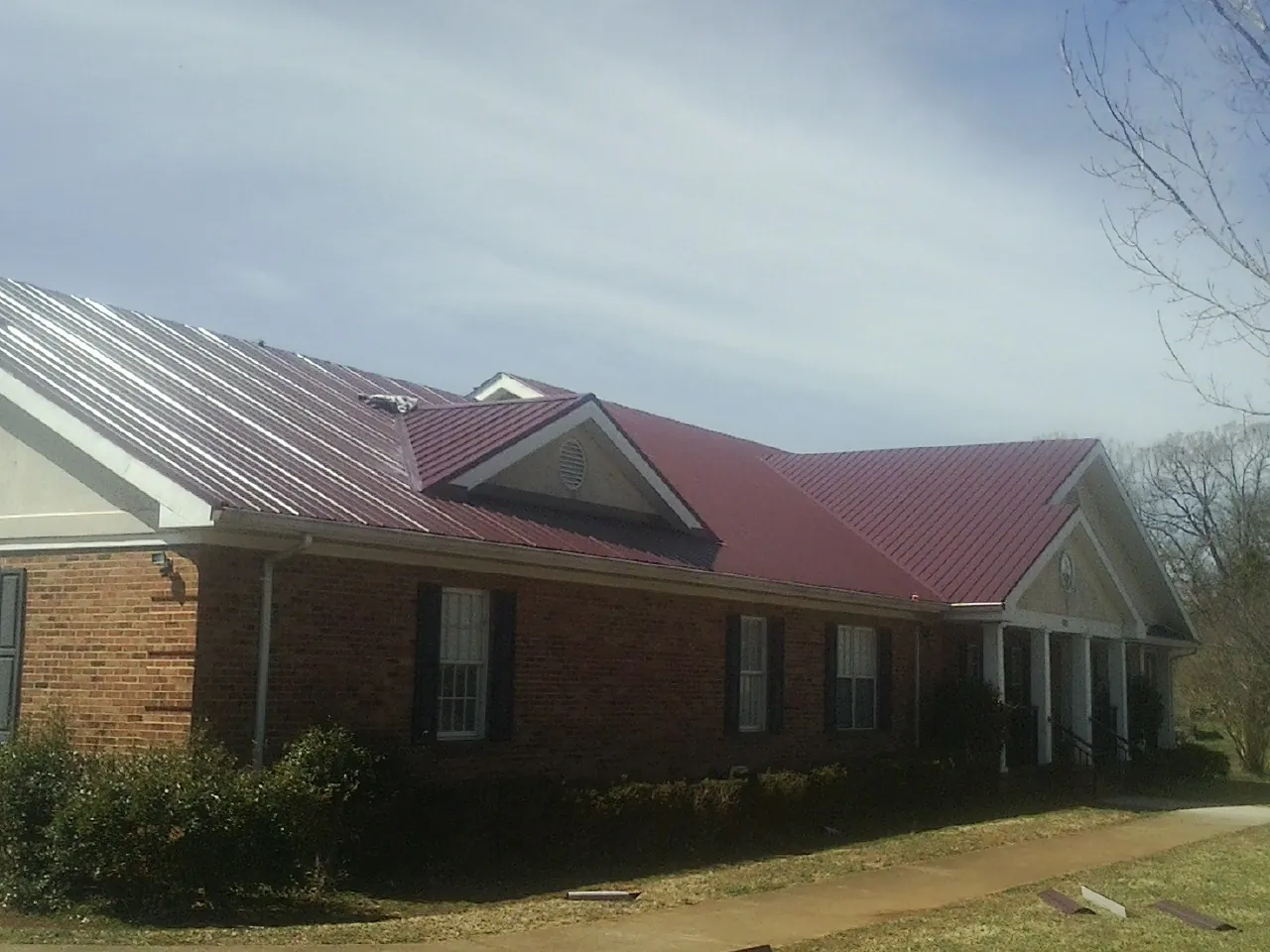 Red metal roof with gabled entries on a long brick building, from a Hail Damage Roof Repair job in Peshtigo