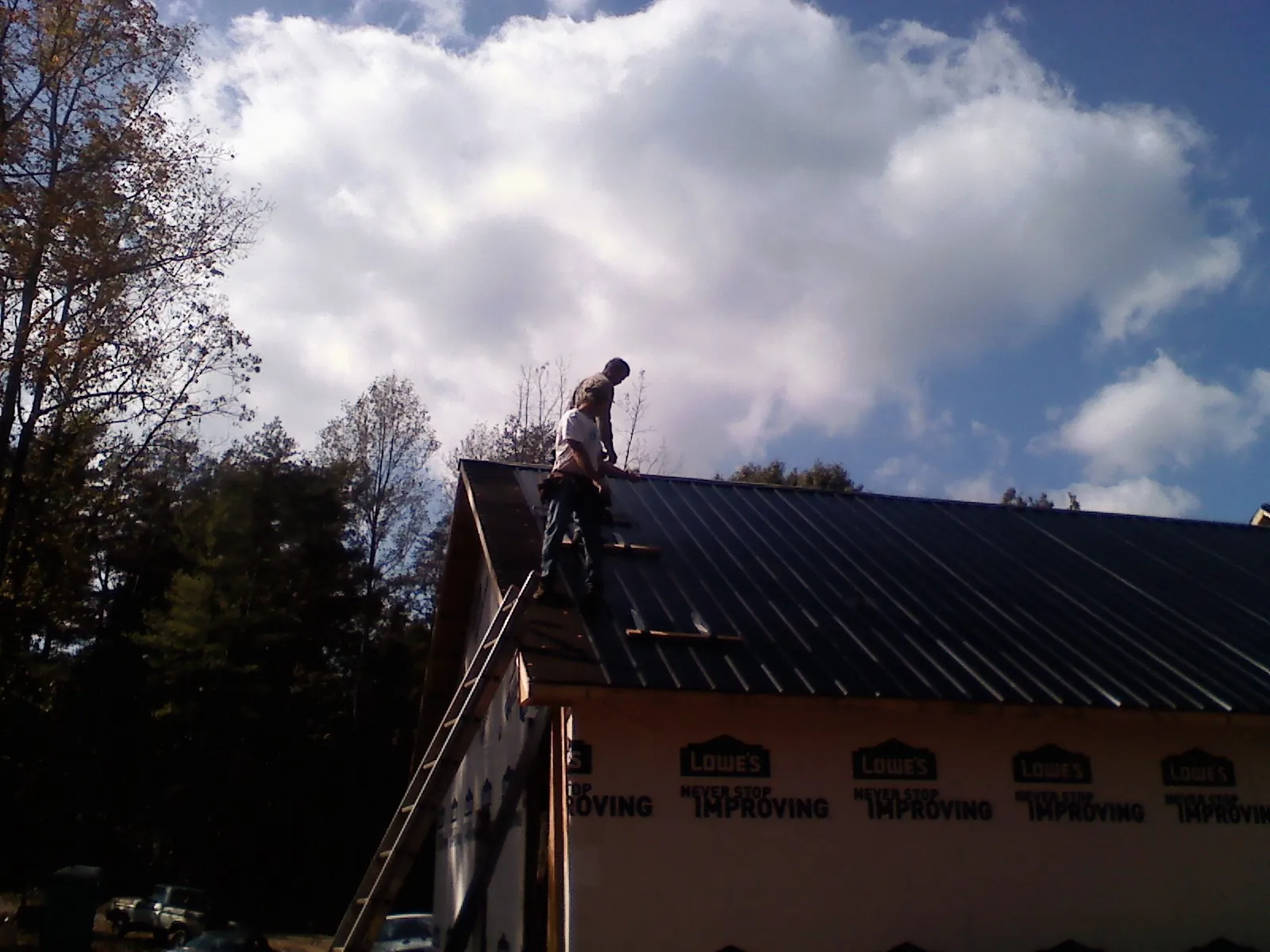 Roofer fastening dark metal panels high against a cloudy sky, from a Roof Inspection job in Peshtigo