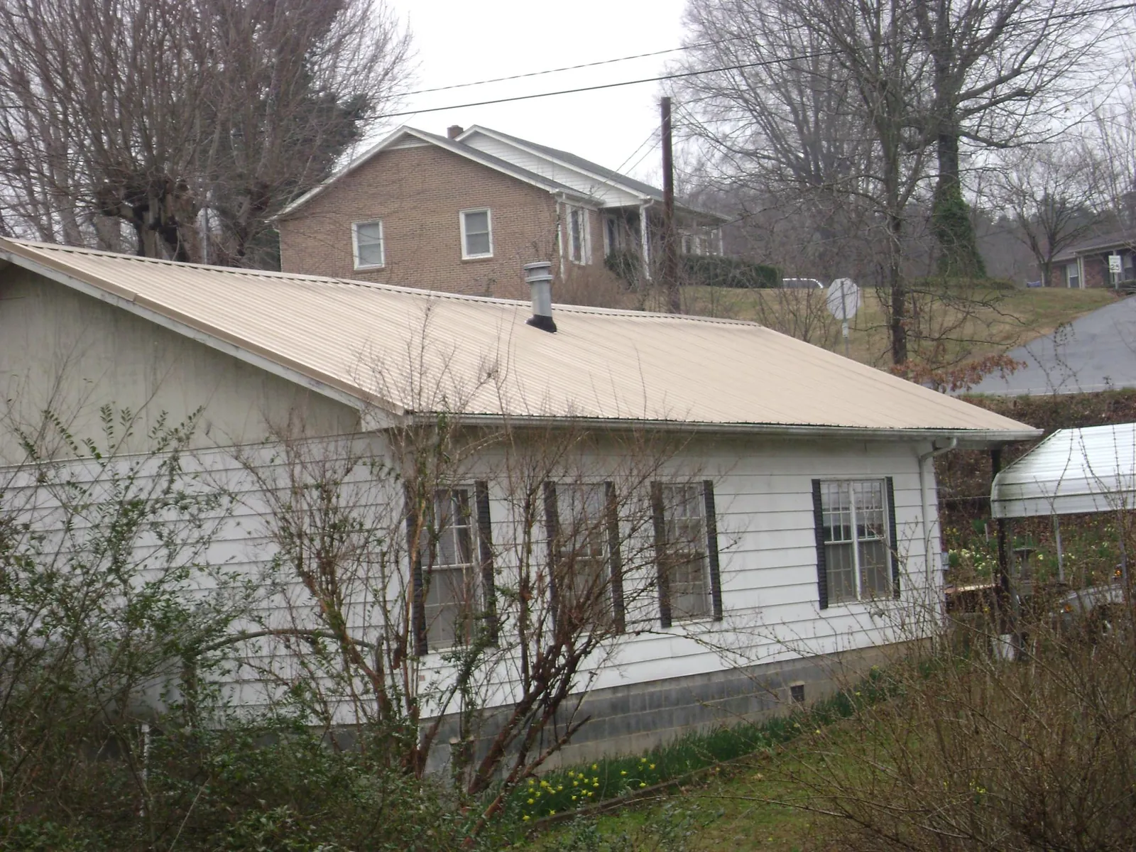 Tan metal roof on a white sided house set into a hillside — Commercial Roofing by Roofing Brothers in Peshtigo