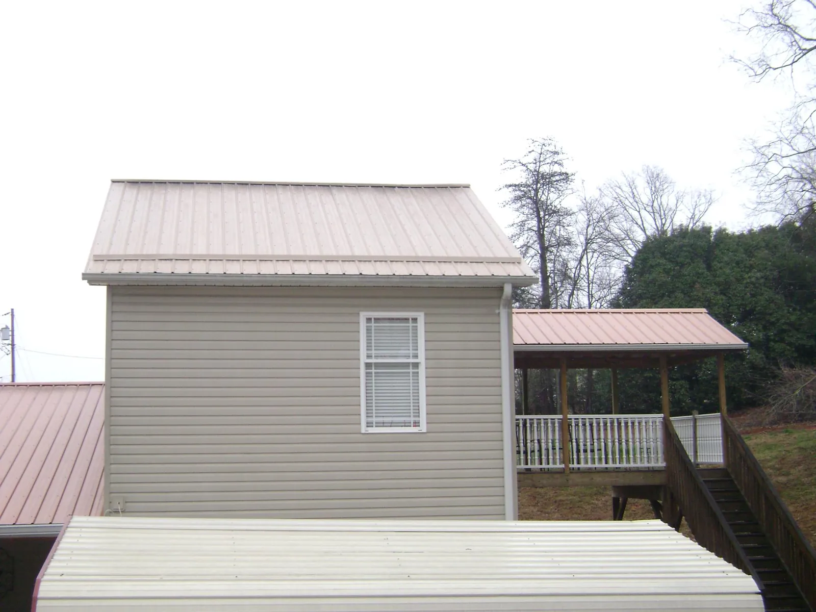 Tan metal roofs on a two story addition and attached porch, from a Roof Replacement job in Peshtigo