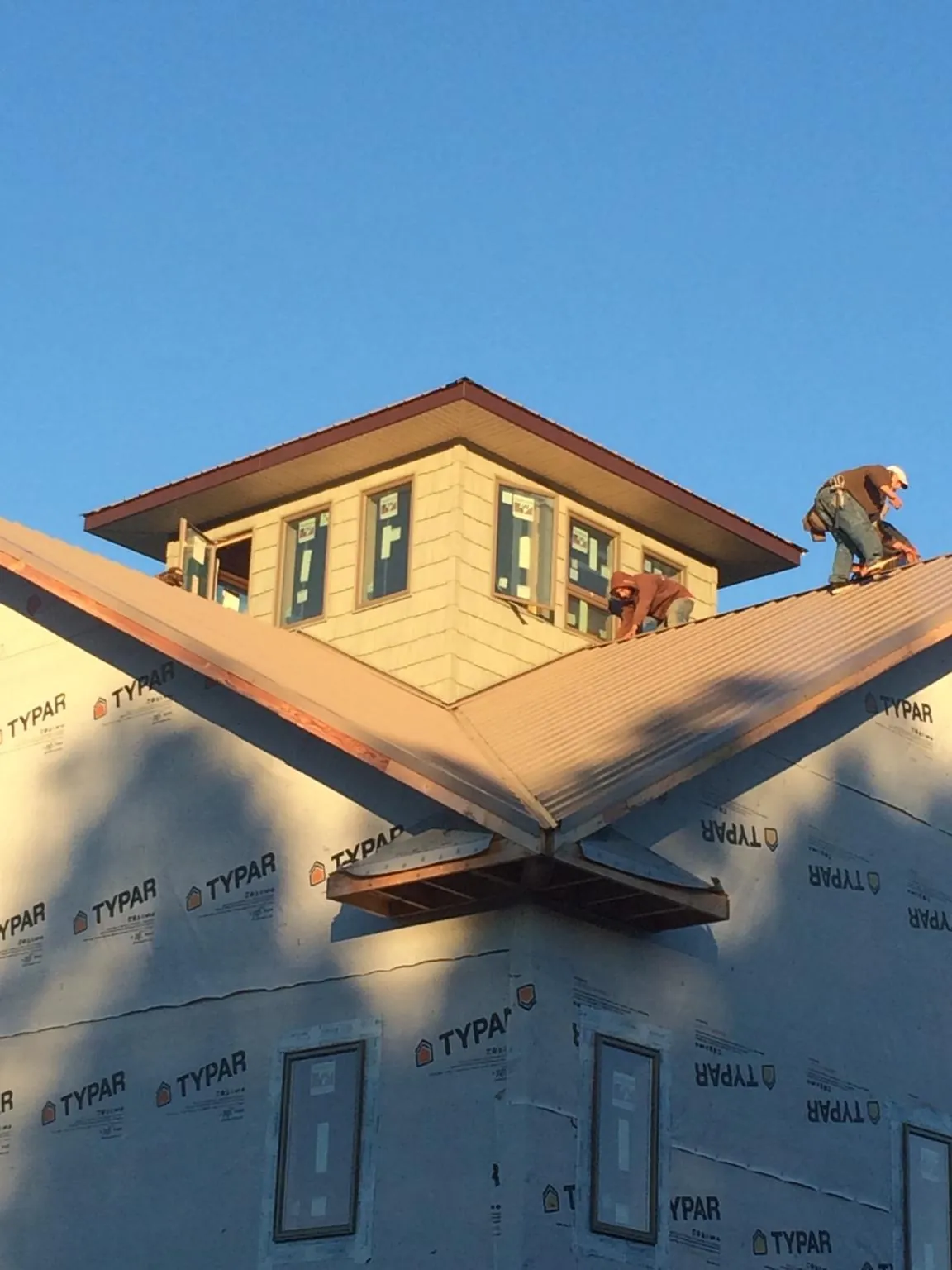 Roofers working around a rooftop cupola on a new metal roof at sunset — Roof Waterproofing in Peshtigo by Roofing Brothers
